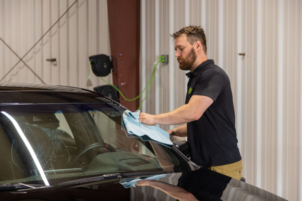 Heartland Dent Shop detailer hand-drying a dark vehicle with a microfiber towel in the Tulsa shop