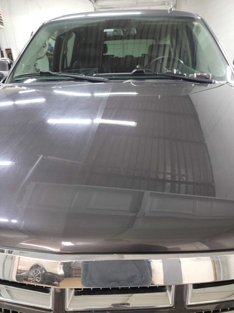 Hood of a dark SUV showing swirl-marked paint on one side