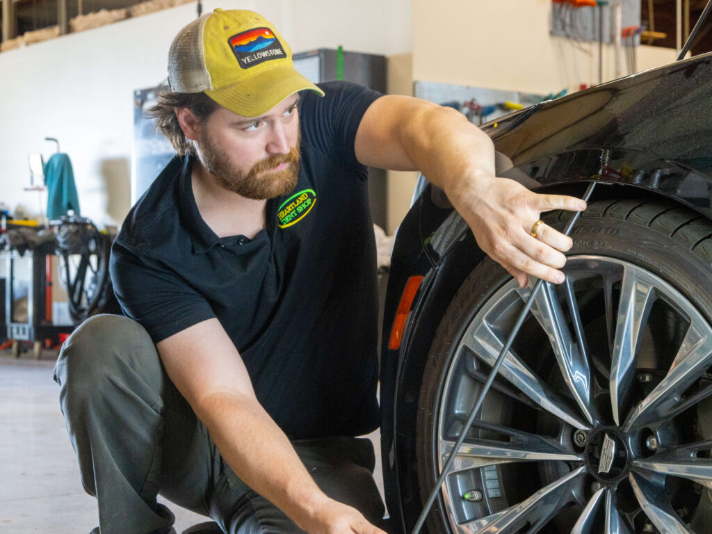 paintless-dent-repair-technician-tulsa - Heartland Dent Shop Heartland Dent Shop technician using a pointless dent repair rod behind the fender of a black Cadillac.